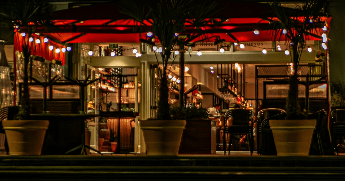 Evening view from outside looking into a restaurant with warm lighting and a cozy atmosphere.